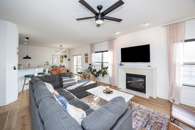 living room featuring light wood finished floors, a fireplace with flush hearth, baseboards, and a ceiling fan