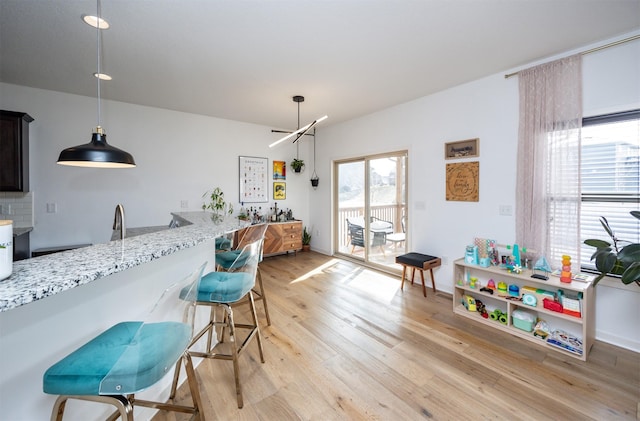 kitchen featuring a kitchen bar, light stone countertops, decorative light fixtures, and light wood-style floors