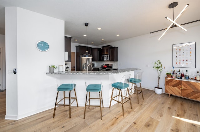 kitchen with light stone counters, a peninsula, a breakfast bar, light wood-style floors, and appliances with stainless steel finishes