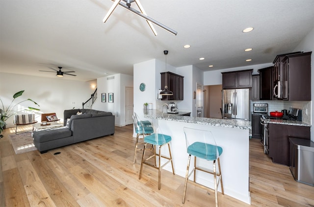 kitchen with a kitchen breakfast bar, dark brown cabinets, light wood-style floors, stainless steel appliances, and a peninsula