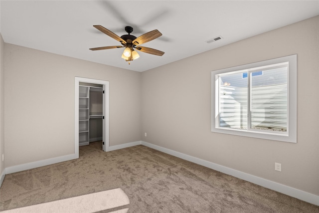 unfurnished bedroom featuring light carpet, a walk in closet, a closet, and ceiling fan