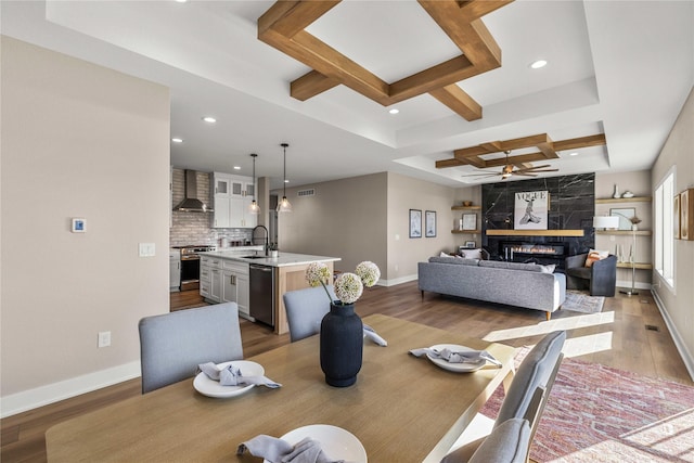 dining area featuring beam ceiling, coffered ceiling, a fireplace, and light hardwood / wood-style floors