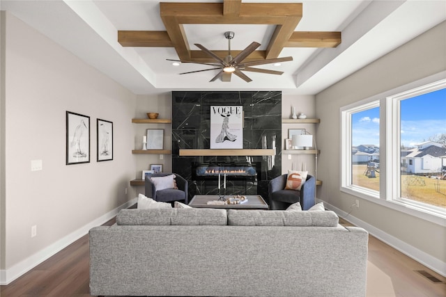 living room with coffered ceiling, hardwood / wood-style floors, a premium fireplace, and ceiling fan