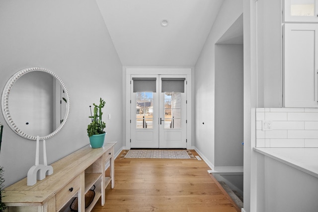 doorway to outside with french doors, baseboards, vaulted ceiling, and light wood finished floors