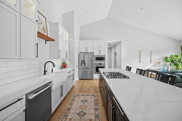 kitchen featuring light wood-style flooring, a sink, appliances with stainless steel finishes, white cabinets, and vaulted ceiling