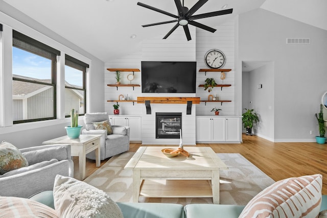 living room featuring ceiling fan, a large fireplace, high vaulted ceiling, and light hardwood / wood-style floors