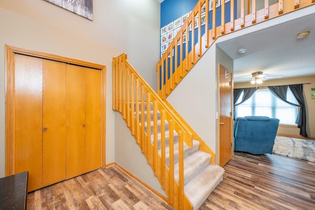 stairs with wood finished floors, ceiling fan, and a high ceiling