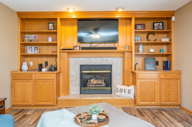 living room featuring a tile fireplace, baseboards, and wood finished floors