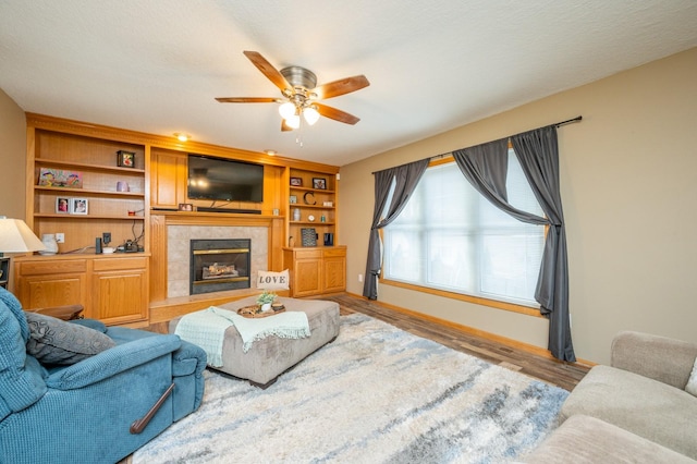 living area with a tile fireplace, a ceiling fan, and wood finished floors