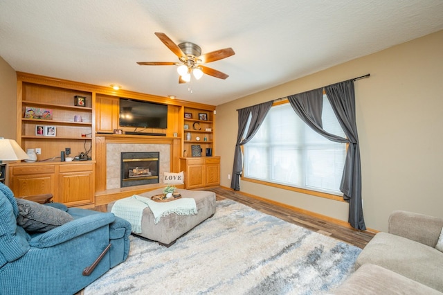 living area with baseboards, wood finished floors, a ceiling fan, and a fireplace