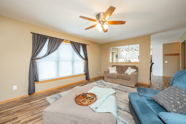 living area featuring wood finished floors, baseboards, and ceiling fan with notable chandelier