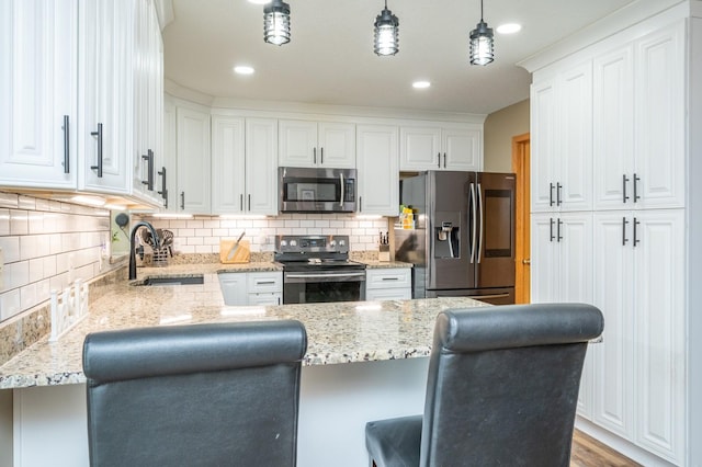 kitchen with a sink, a kitchen breakfast bar, white cabinetry, appliances with stainless steel finishes, and a peninsula