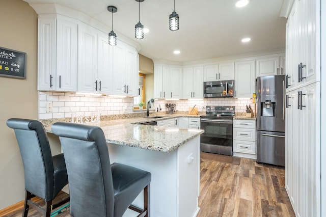 kitchen with a breakfast bar area, wood finished floors, a peninsula, stainless steel appliances, and white cabinetry