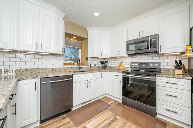 kitchen featuring a sink, light wood-style floors, appliances with stainless steel finishes, a textured ceiling, and white cabinetry