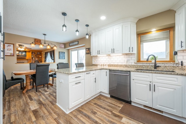 kitchen featuring visible vents, a sink, stainless steel dishwasher, wood finished floors, and a peninsula