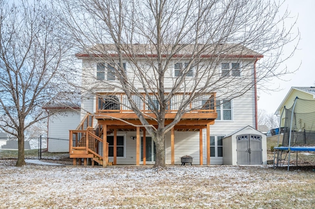 snow covered house featuring a trampoline, fence, a deck, an outbuilding, and a storage unit