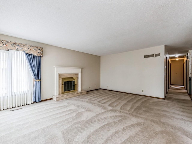 unfurnished living room with a high end fireplace, light colored carpet, visible vents, and a textured ceiling