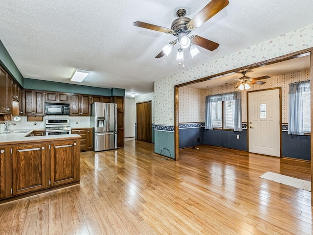 kitchen featuring a textured ceiling, light wood-style flooring, light countertops, appliances with stainless steel finishes, and wallpapered walls