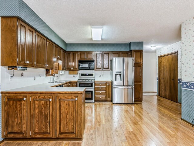 kitchen featuring sink, stainless steel appliances, light hardwood / wood-style floors, a textured ceiling, and kitchen peninsula