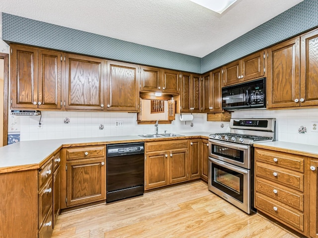 kitchen with light wood-style flooring, brown cabinets, light countertops, black appliances, and a sink