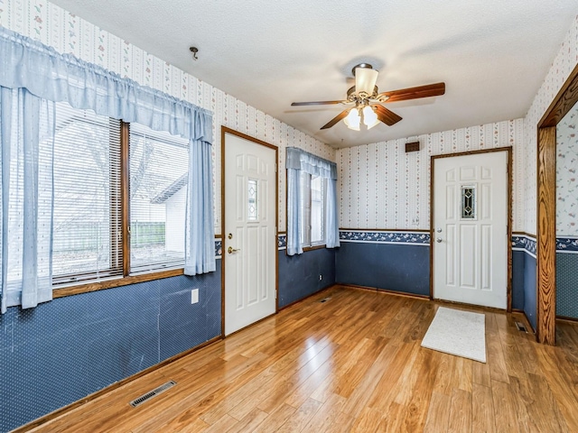 entrance foyer with a textured ceiling, wood finished floors, visible vents, and wallpapered walls