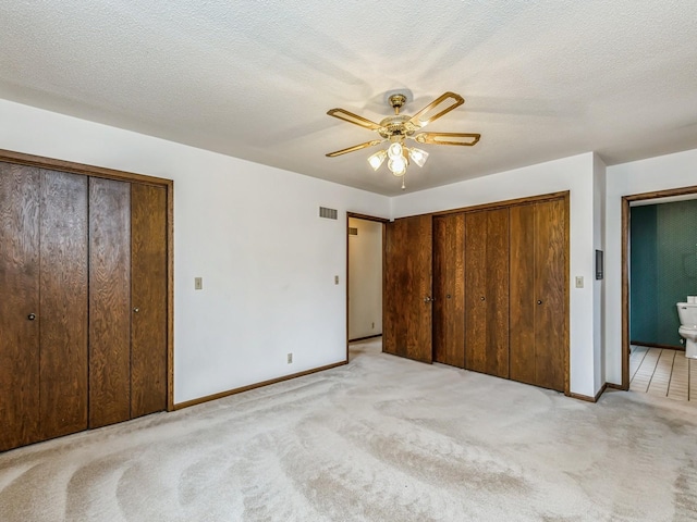 unfurnished bedroom featuring multiple closets, visible vents, light carpet, and a textured ceiling