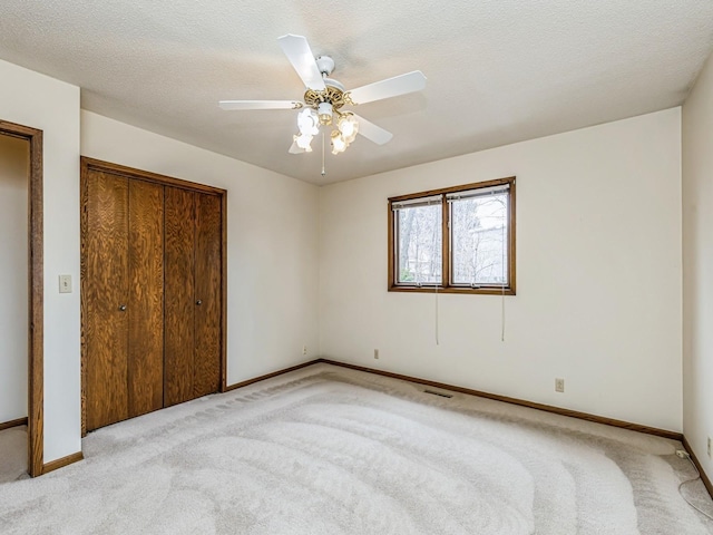 unfurnished bedroom with a textured ceiling, a closet, baseboards, and light colored carpet