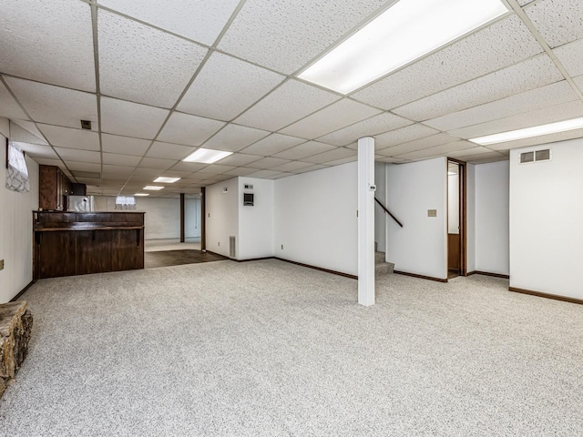 finished below grade area featuring a paneled ceiling, visible vents, light carpet, baseboards, and stairs