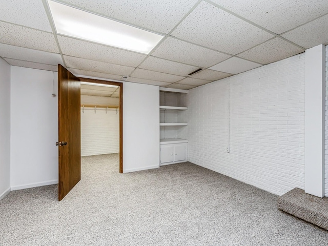 finished basement featuring brick wall, carpet, baseboards, and a drop ceiling