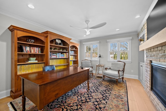 office space with crown molding, a fireplace, ceiling fan, and light hardwood / wood-style floors