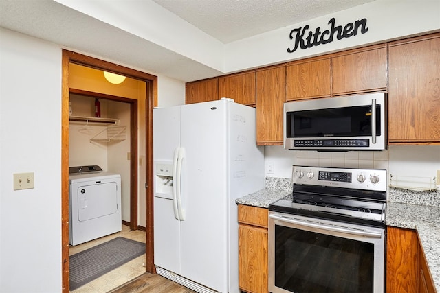 kitchen with appliances with stainless steel finishes, washer / dryer, light stone countertops, a textured ceiling, and light hardwood / wood-style flooring