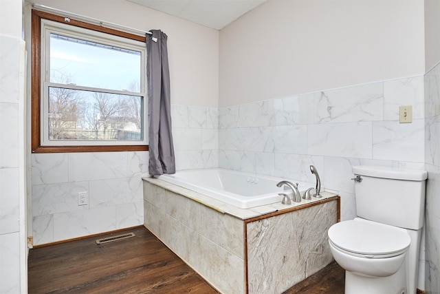 bathroom featuring hardwood / wood-style flooring, tiled bath, tile walls, and toilet