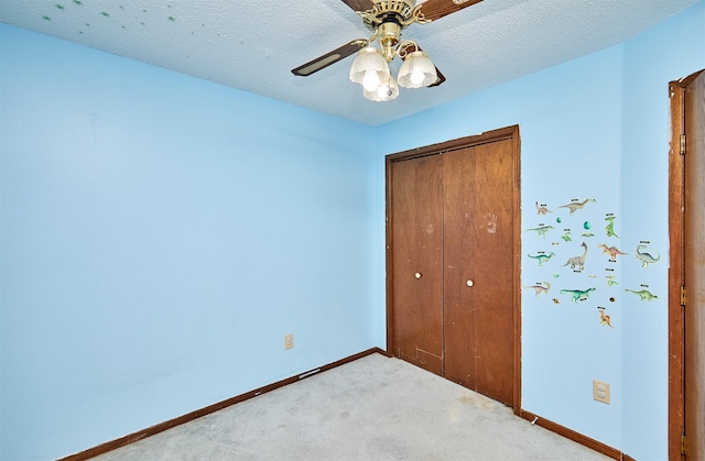 unfurnished bedroom featuring ceiling fan, a closet, light carpet, and a textured ceiling