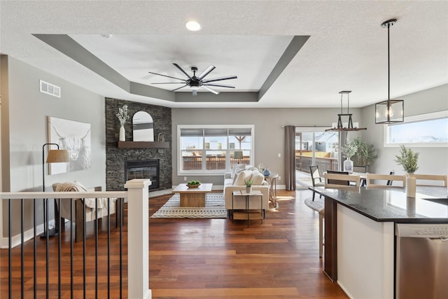 living room featuring a stone fireplace, dark hardwood / wood-style flooring, ceiling fan, a raised ceiling, and a textured ceiling