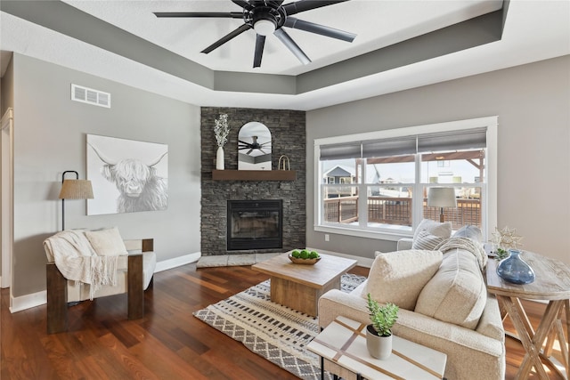 living room with ceiling fan, a tray ceiling, a fireplace, and dark wood-type flooring