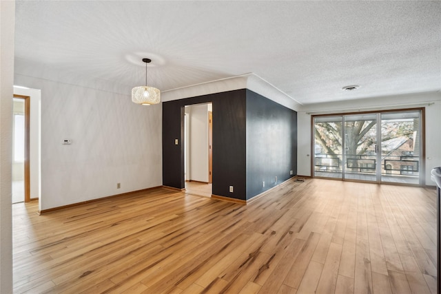 spare room with a notable chandelier, a textured ceiling, and light hardwood / wood-style flooring