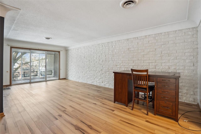 unfurnished office featuring brick wall and light wood-type flooring