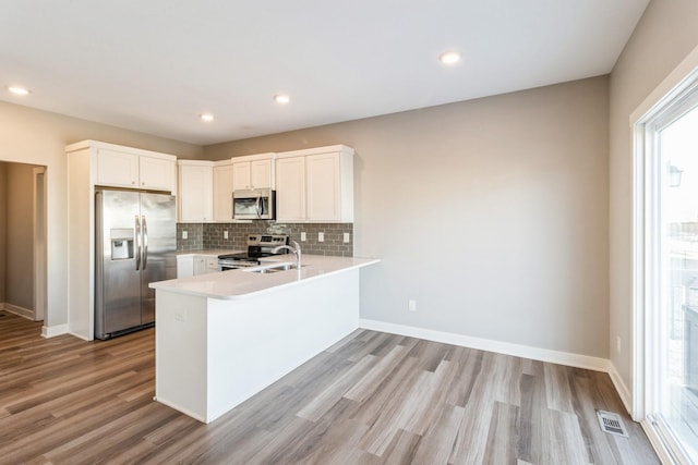 kitchen with white cabinetry, decorative backsplash, light hardwood / wood-style floors, kitchen peninsula, and stainless steel appliances