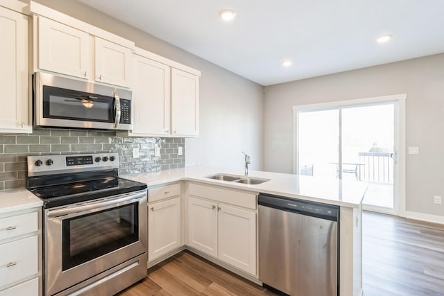 kitchen with sink, white cabinets, kitchen peninsula, stainless steel appliances, and light wood-type flooring