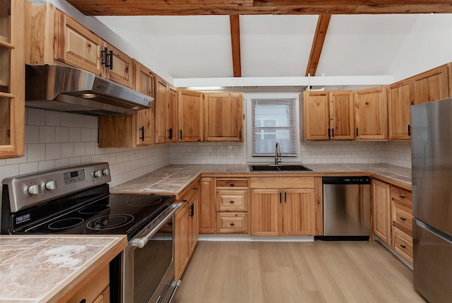 kitchen featuring appliances with stainless steel finishes, sink, backsplash, tile counters, and light wood-type flooring