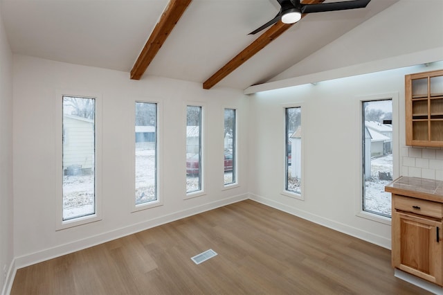 unfurnished dining area with ceiling fan, lofted ceiling with beams, light hardwood / wood-style flooring, and a wealth of natural light