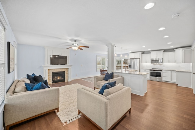 living room with decorative columns, light hardwood / wood-style flooring, a stone fireplace, sink, and ceiling fan