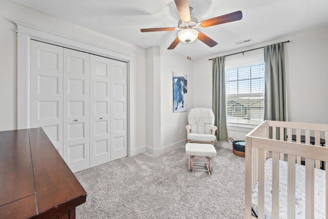 carpeted bedroom featuring a nursery area, ceiling fan, and a closet