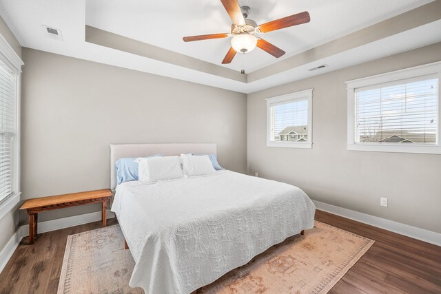 bedroom with dark hardwood / wood-style flooring, ceiling fan, and a tray ceiling