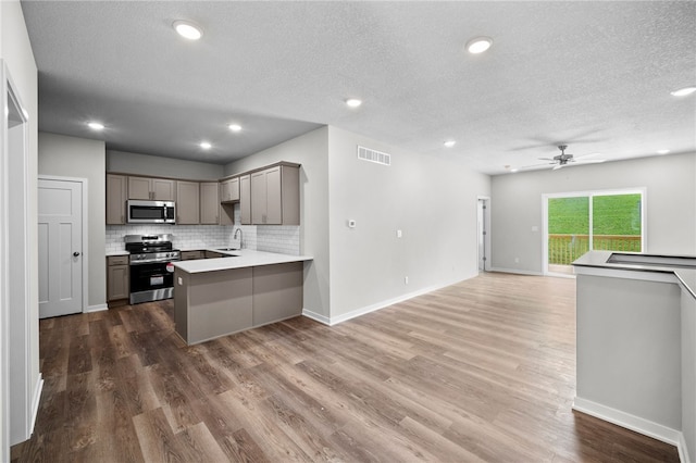 kitchen featuring sink, stainless steel appliances, tasteful backsplash, a textured ceiling, and kitchen peninsula