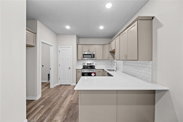 kitchen featuring sink, kitchen peninsula, stainless steel appliances, hardwood / wood-style floors, and backsplash