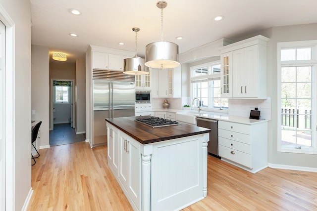 kitchen with wood counters, decorative light fixtures, white cabinetry, a center island, and built in appliances