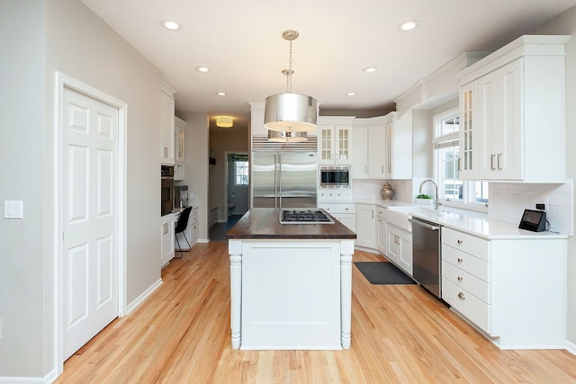 kitchen with built in appliances, white cabinetry, pendant lighting, and a center island