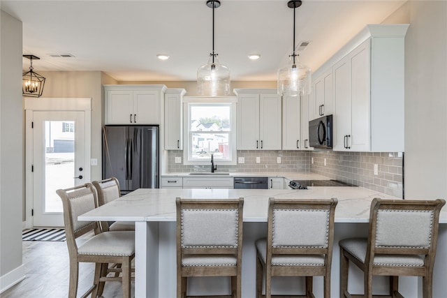 kitchen with a kitchen bar, white cabinetry, hanging light fixtures, appliances with stainless steel finishes, and a kitchen island