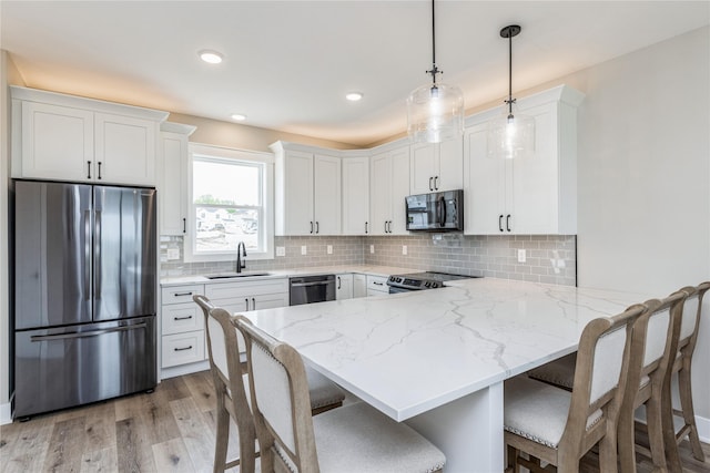 kitchen with white cabinetry, appliances with stainless steel finishes, sink, and decorative light fixtures